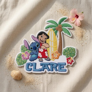 Peut inclure: Un &eacute;cusson brod&eacute; repr&eacute;sentant les personnages Lilo et Stitch &agrave; c&ocirc;t&eacute; d'une planche de surf jaune et d'un palmier. Le motif comprend des fleurs tropicales, des feuilles vertes et le nom CLARE en lettres bleues en bas de l'&eacute;cusson.