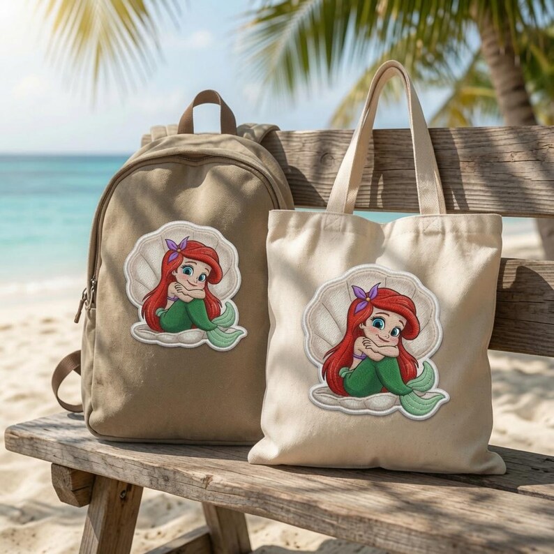 May include: A tan canvas backpack and a matching off-white canvas tote bag, both featuring a centred embroidered patch of a cartoon mermaid with long red hair and a green tail, sitting inside a large white seashell with a purple hair accessory.