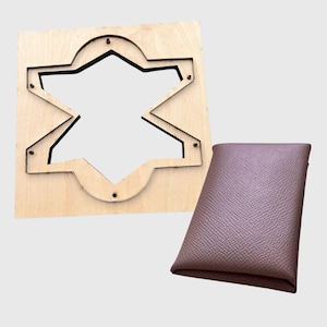 Può includere: Un fustellato in legno a forma di stella con un bordo decorativo e un astuccio in pelle marrone. Il fustellato è di colore marrone chiaro ed è realizzato in legno. L'astuccio ha una forma rettangolare e una superficie strutturata.