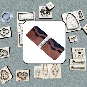 May include: A bi-fold wallet featuring a brown and navy blue color-blocked design with wavy edges on the card slots. The wallet is open and contains a single one-hundred dollar bill. The wallet is surrounded by various metal cutting dies.