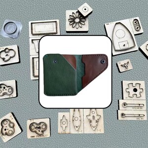 May include: A bi-fold leather wallet featuring a dark green exterior pocket and a brown interior section, secured with a single metal snap button. The wallet is surrounded by various wooden and metal craft cutting dies on a textured gray surface.