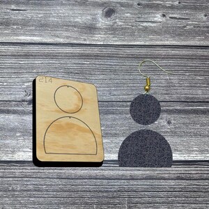 May include: A wooden die-cut template with the number 214 and a design for earrings. The earrings are dark gray with a textured pattern, featuring a small circle above a semi-circle, suspended from a gold-colored hook.