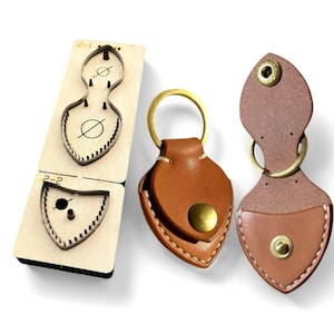 May include: A wooden die-cut tool and two brown leather keychains. The die-cut tool has two sections with shield-shaped cutouts. The keychains are made of brown leather with brass hardware, including a snap closure and a key ring.