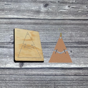 Puede incluir: Una herramienta de corte de madera y un pendiente de cuero marrón claro. La herramienta de corte es de color marrón claro y tiene forma triangular con un diseño recortado. El pendiente tiene forma triangular con un gancho dorado.