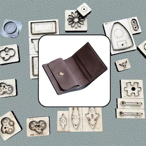May include: A brown leather wallet with a single silver snap button closure, surrounded by various metal cutting dies on wooden blocks, including shapes like a flower, puzzle piece, cloud, and geometric forms on a textured gray surface.