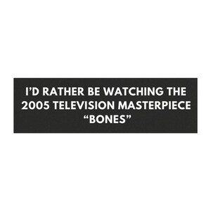 Könnte beinhalten: Ein schwarzes rechteckiges Schild mit weißem Text: "I'D RATHER BE WATCHING THE 2005 TELEVISION MASTERPIECE 'BONES'". Das Schild ist eine einfache, kühne Aussage.