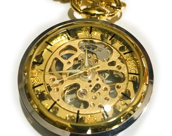 May include: A gold pocket watch with a skeletonized face, revealing the intricate inner workings of the watch. The watch has a silver rim and a gold chain.
