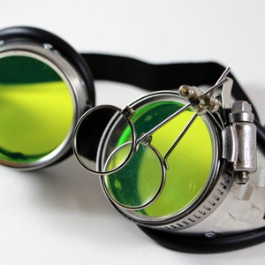 May include: Silver steampunk goggles with green lenses and a magnifying glass attached to the side.