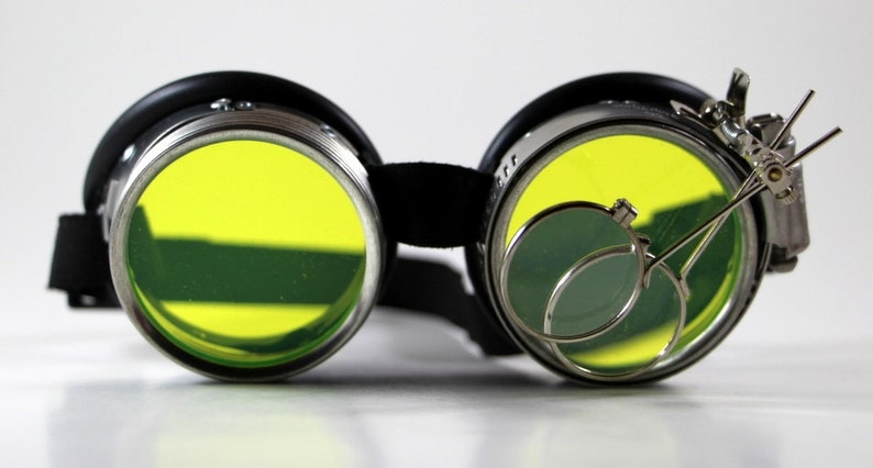 May include: Black steampunk goggles with yellow lenses and a silver magnifying glass attachment.