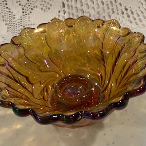 Peut inclure: Un bol en verre carnaval couleur souci avec une finition irisée et un bord festonné. Le bol présente une indentation circulaire centrale et un motif texturé en forme de feuille rayonnant du centre vers le bord ondulé aux reflets sombres.
