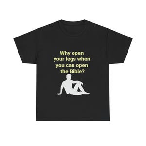 Op de afbeelding: Een zwart t-shirt met korte mouwen en de tekst "Why open your legs when you can open the Bible?" in een lichtgele kleur boven een witte silhouetafbeelding van een persoon die op de grond zit met één been gebogen.