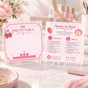 May include: Two square pink and white cards displayed on clear stands. The left card features the text Pretty Nails, a strawberry graphic, and social media icons. The right card provides instructions for nail application and removal with text.