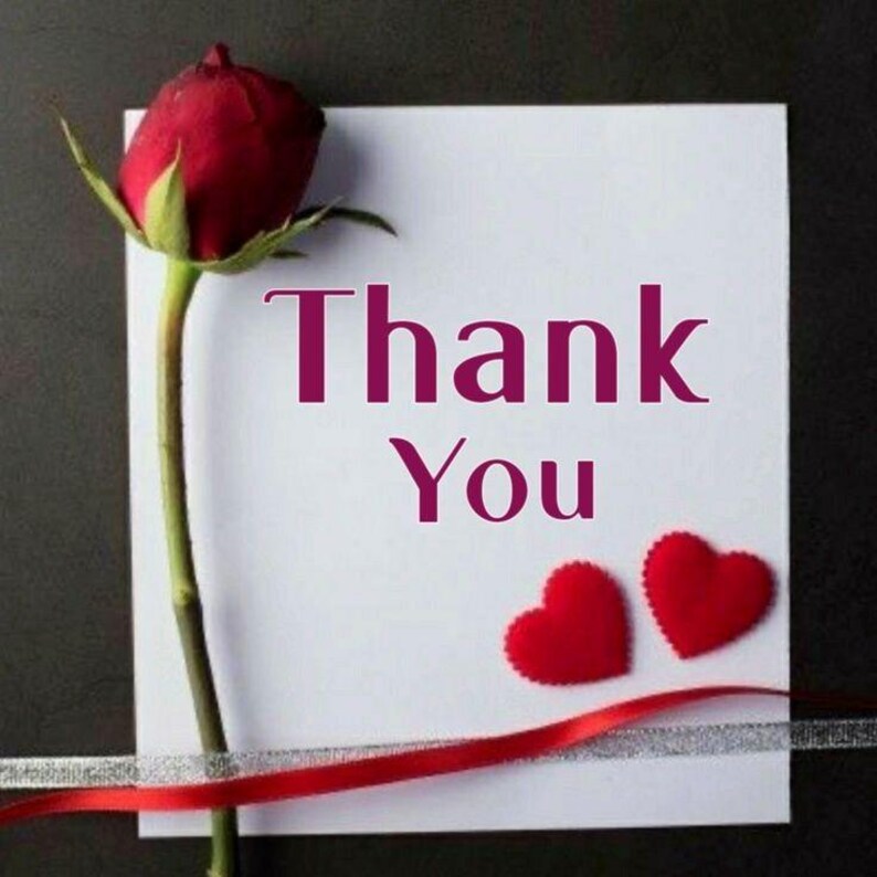 May include: A white card with the words "Thank You" in a deep pink font, accompanied by two red heart-shaped decorations and a red rose. A red ribbon and silver ribbon are also present.