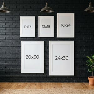 May include: Five white framed art prints of varying sizes are displayed on a black brick wall. The sizes are 11x17 inches, 12x18 inches, 16x24 inches, 20x30 inches, and 24x36 inches. The room has a modern aesthetic with a wooden floor and a dark gray armchair.