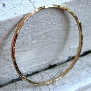 K&ouml;nnte beinhalten: Ein goldfarbenes Armreif-Armband mit geh&auml;mmerter Textur.