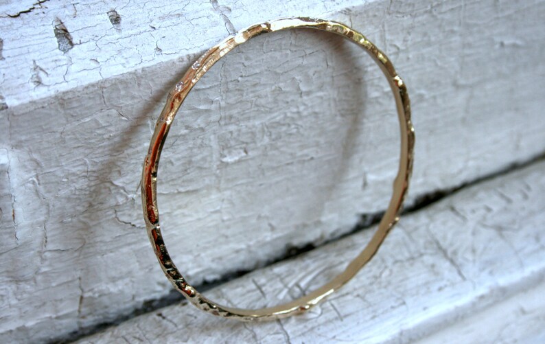 K&ouml;nnte beinhalten: Ein goldfarbenes Armreif-Armband mit geh&auml;mmerter Textur.