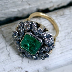 May include: A gold ring featuring a large emerald green gemstone surrounded by a halo of smaller diamonds.