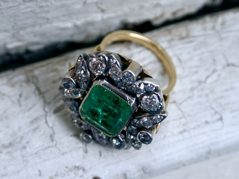 May include: A gold ring featuring a large emerald green gemstone surrounded by a halo of smaller diamonds.