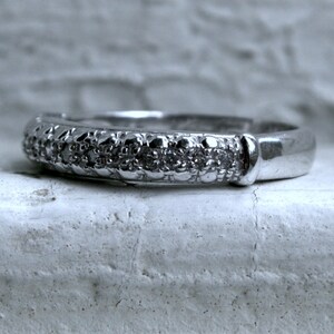 May include: A silver band ring with a row of small diamonds set in the band.
