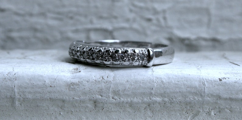 May include: A silver band ring with a row of small diamonds set in the band.