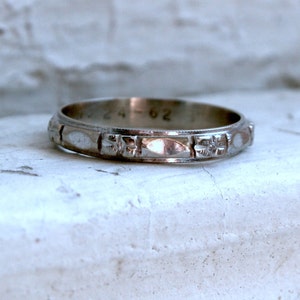 May include: A silver wedding band with a decorative pattern of small flowers and ovals. The band is inscribed with the date "24-62".