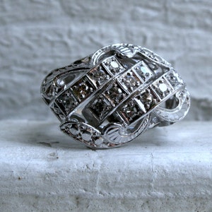 May include: A silver ring with a geometric design featuring a cluster of small diamonds.