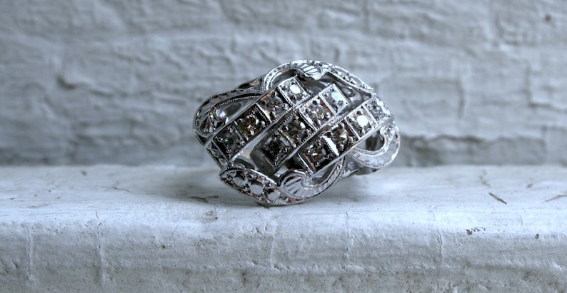 May include: A silver ring with a geometric design featuring a cluster of small diamonds.