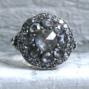 May include: A silver ring with a large, faceted, clear gemstone surrounded by smaller, faceted, gray gemstones.