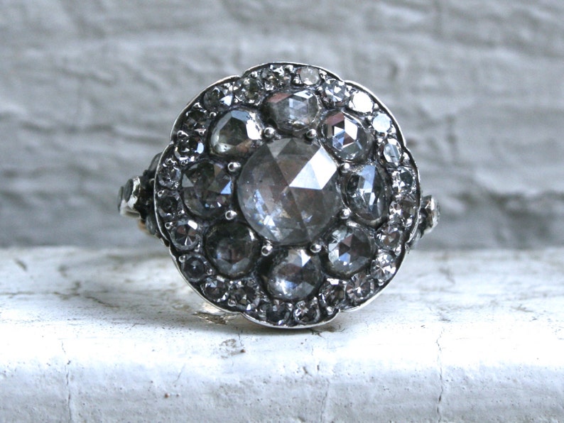 May include: A silver ring with a large, faceted, clear gemstone surrounded by smaller, faceted, gray gemstones.