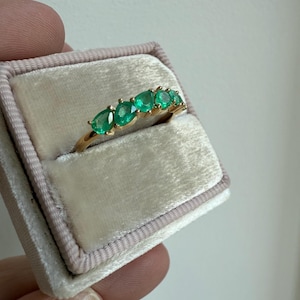 May include: A gold band ring with seven emerald green gemstones set in a row.