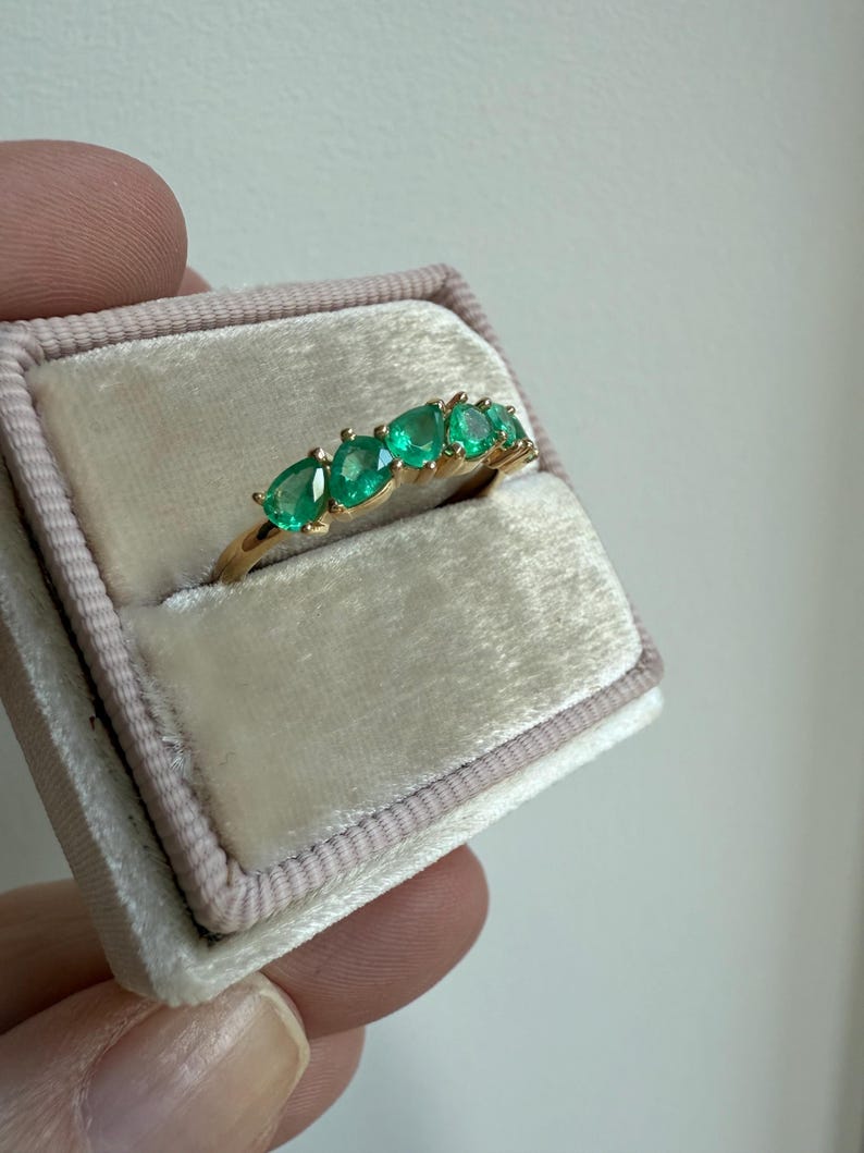 May include: A gold band ring with seven emerald green gemstones set in a row.