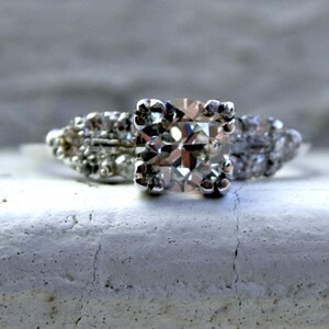 May include: A silver engagement ring featuring a large, square-cut diamond surrounded by smaller diamonds.