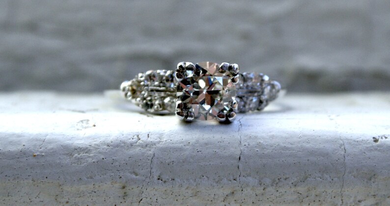 May include: A silver engagement ring featuring a large, square-cut diamond surrounded by smaller diamonds.