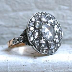 May include: A silver ring with a large, round, faceted diamond surrounded by smaller diamonds. The ring has a gold band.