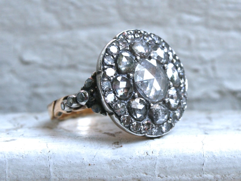 May include: A silver ring with a large, round, faceted diamond surrounded by smaller diamonds. The ring has a gold band.
