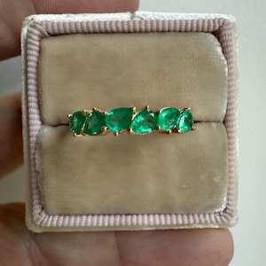 May include: A gold band ring with a row of emerald green pear-shaped gemstones.