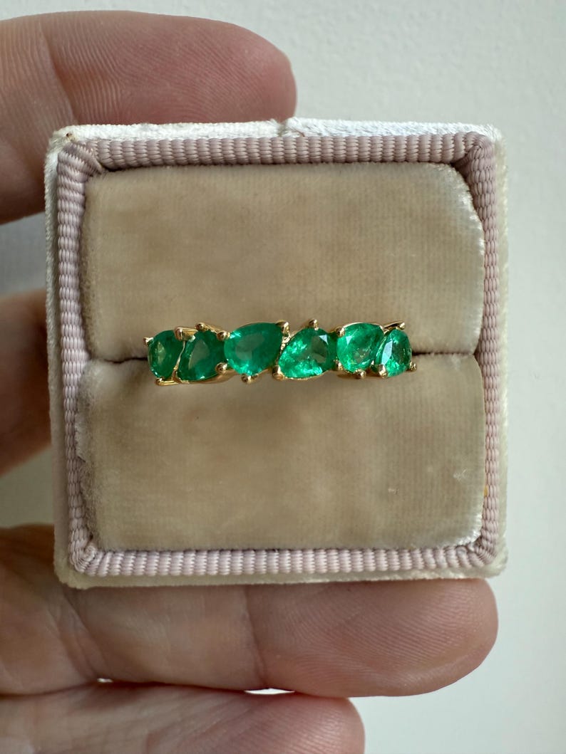 May include: A gold band ring with a row of emerald green pear-shaped gemstones.