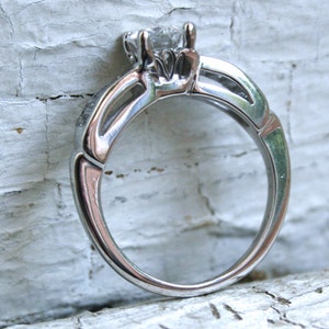 K&ouml;nnte beinhalten: Ein silberner Verlobungsring mit einem einzelnen, klaren, runden Brillanten in einer Krappenfassung. Die Ringschiene ist in einem zarten, gedrehten Design gehalten.