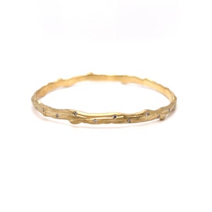 K&ouml;nnte beinhalten: Ein goldenes Armreif-Armband mit einem strukturierten, ast&auml;hnlichen Design und kleinen, klaren Diamanten, die &uuml;ber die Oberfl&auml;che verteilt sind.