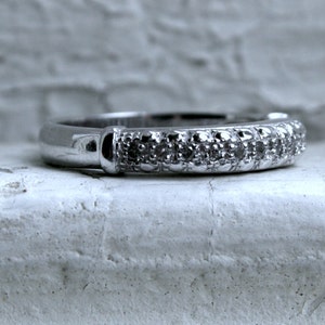 May include: A silver band ring with a row of small diamonds set in the band.