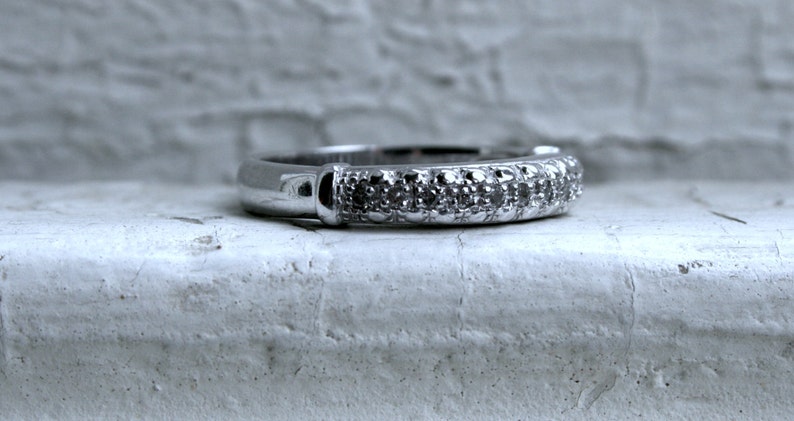 May include: A silver band ring with a row of small diamonds set in the band.