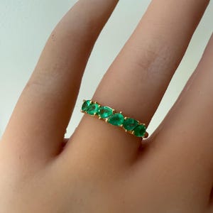 May include: A gold band ring with a row of emerald green oval-shaped stones.