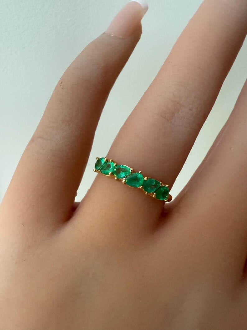 May include: A gold band ring with a row of emerald green oval-shaped stones.