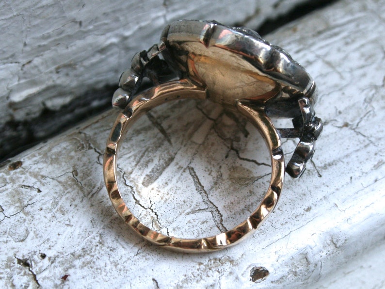 May include: A gold and silver ring with a large, round, faceted stone set in the center. The ring has a textured band and a decorative design on the side.