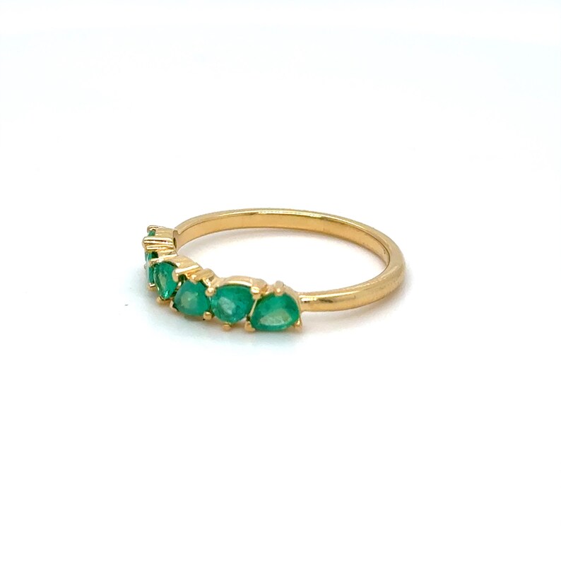 May include: A gold band ring with a row of emerald green gemstones.