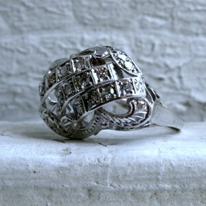 May include: A silver ring with a intricate design featuring a cluster of small diamonds set in a geometric pattern.