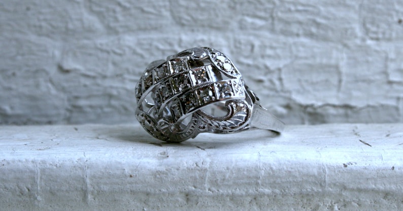 May include: A silver ring with a intricate design featuring a cluster of small diamonds set in a geometric pattern.