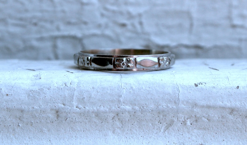 May include: A silver wedding band with a delicate floral design.