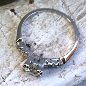 May include: A silver engagement ring featuring a round, clear centre stone and a band decorated with smaller diamonds.