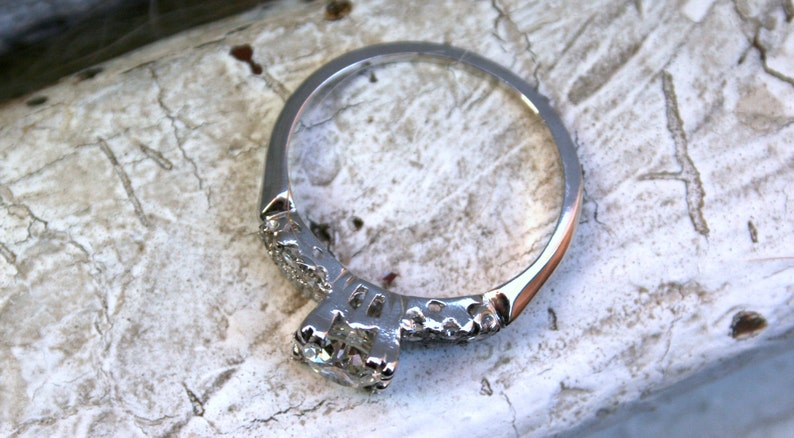 May include: A silver engagement ring featuring a round, clear centre stone and a band decorated with smaller diamonds.
